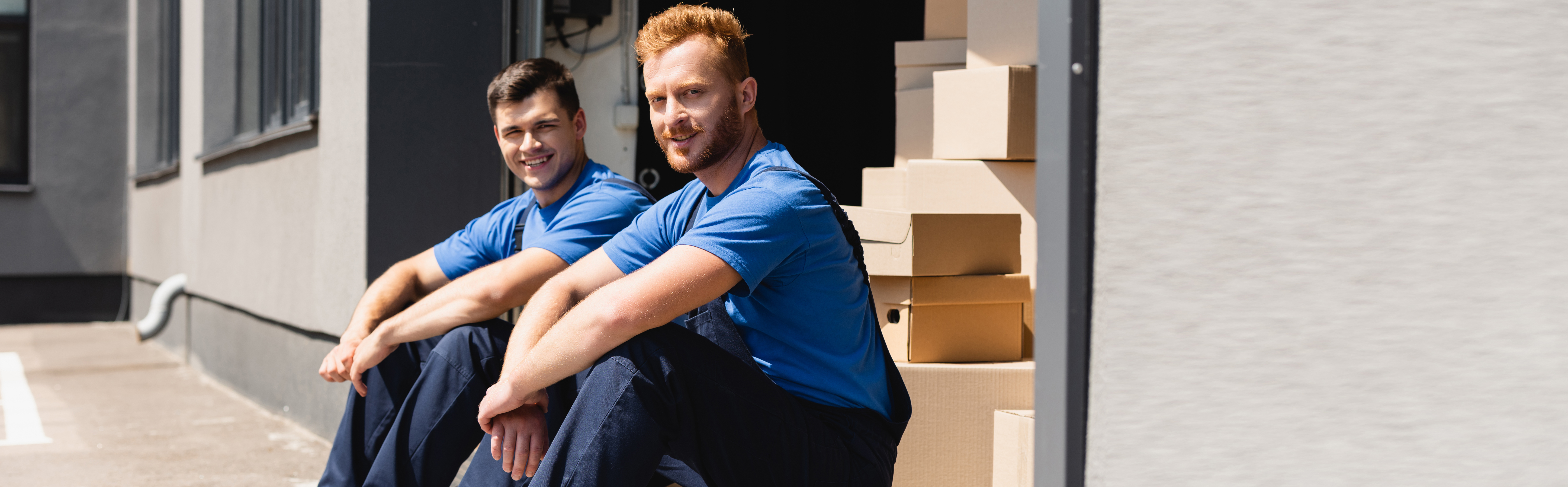 Two Sol crew members in uniform sitting outside a job, boxes stacked beside them